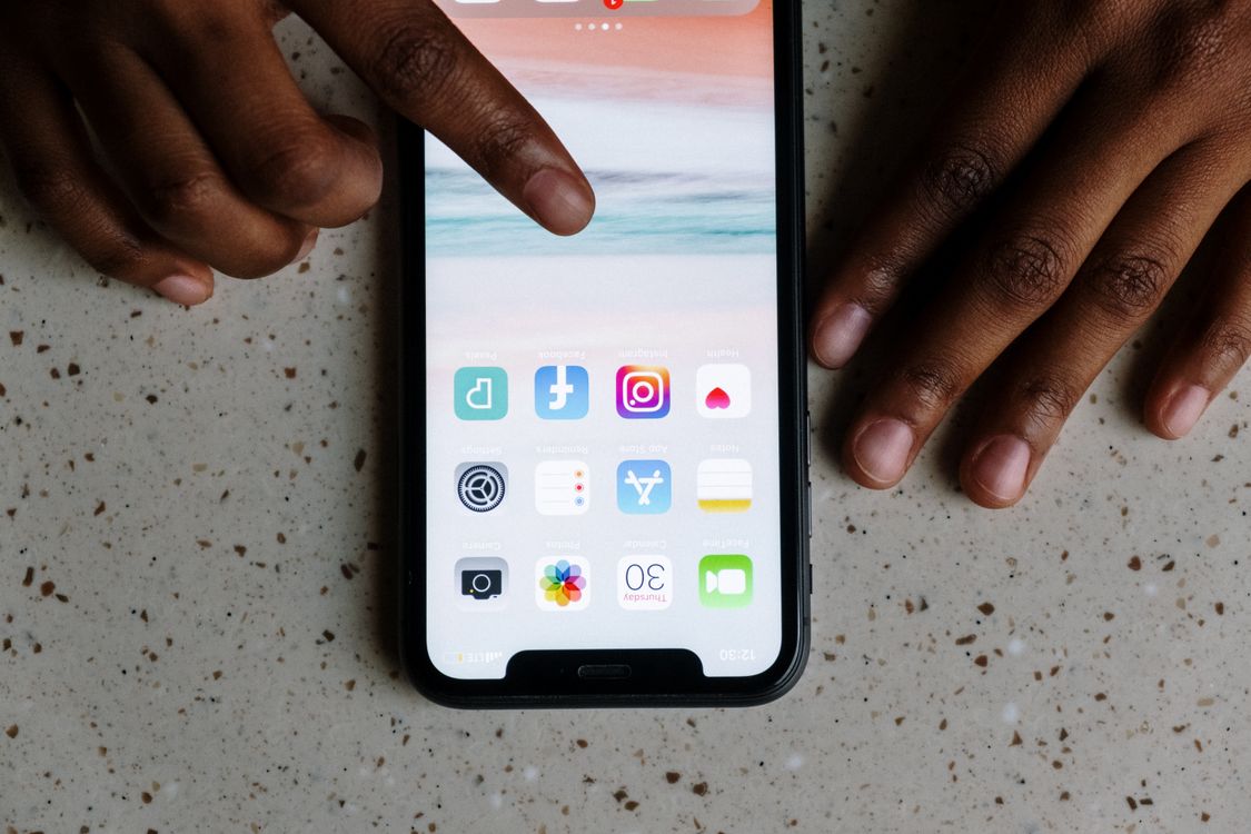 Tangan memegang smartphone dengan ikon aplikasi di layar sentuh